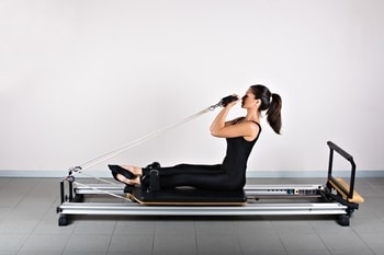 woman doing seated bicep curl pilates exercises on reformer